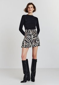 Schwarzes Langarmoberteil mit Drapierung, kombiniert mit einem Minirock im Zebra-Print mit einem Knoten an der Taille. Schwarze kniehohe Stiefel.