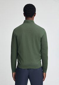 Grön stickad tröja med ribbad krage och ärmslut, som har en lätt textur. Baksidan visar en enkel, sömlös design.