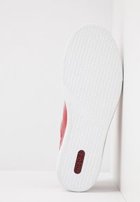 Baskets rouges avec une tige en cuir texturé, une semelle en caoutchouc blanche et un motif côtelé distinct au bas. Présentant un détail logo sur le côté.