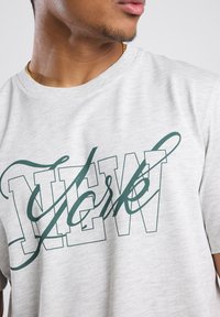 Grijze katoenen t-shirt met het woord "NEW YORK" in donkergroene letters. Het ontwerp heeft een cursieve accent en een klassieke ronde hals.