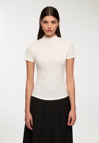 Biała, prążkowana bluzka z krótkim rękawem i wysokim ko�łnierzem, dopasowany krój, gładka tekstura, zestawiona z czarną spódnicą plisowaną.
