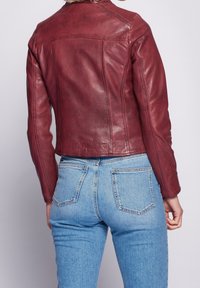 Giacca di pelle bordeaux con un design aderente, texture liscia e cuciture a contrasto, abbinata a jeans in denim azzurro chiaro.