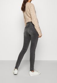 Jeans de tiro alto de color gris oscuro, ajustados, con dos bolsillos traseros. Combinados con un suéter de punto beige claro y zapatillas blancas.