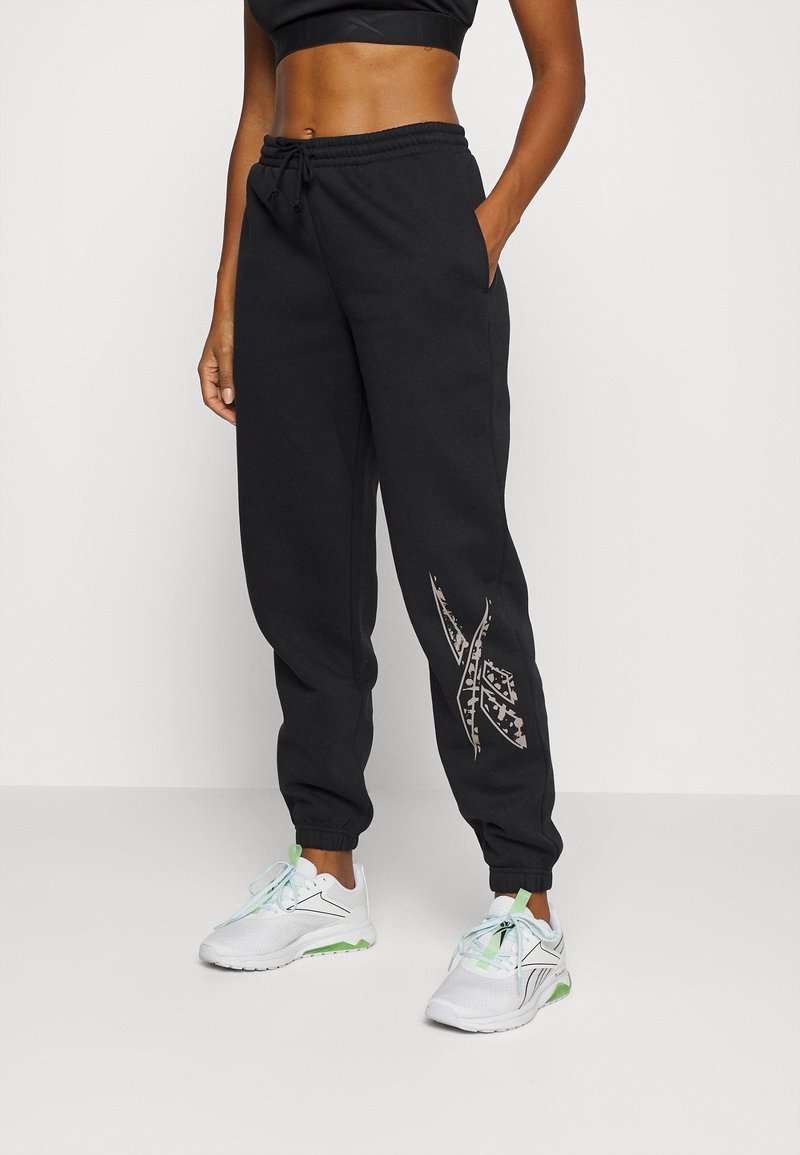 Černé tepláky vyrobené z měkké látky, s tapered nohavicemi, elastickým pasem se šňůrkou a grafickým designem na levé nohavici.