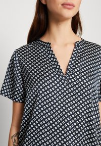 Top azzurro scuro a maniche corte con scollatura a V, caratterizzato da un motivo a rombi bianchi. Tessuto morbido e leggero con una vestibilità comoda.
