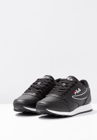 Black athletic shoes with a smooth leather upper, white soles, and classic lace-up design. FILA logo in silver and red accents.