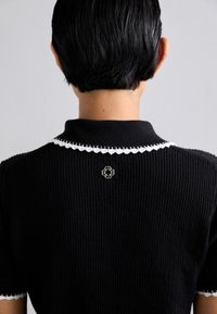 Maglietta nera a costine a maniche corte con colletto in pizzo bianco e decorativo hardware a forma di fiore argentato sul collo posteriore.