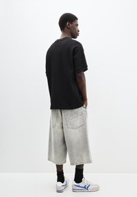 Tricou negru oversized, pantaloni scurți din denim gri cu detalii texturate, adidași albi cu accente albastre, șosete negre, vedere din lateral.