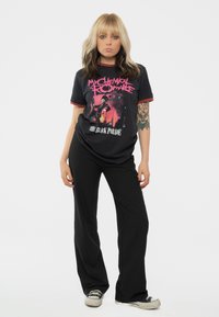 Black graphic t-shirt with red trim featuring a colorful design and text. Paired with black pants and retro-style sneakers.
