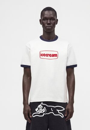 Homme portant un t-shirt blanc avec un texte rouge "icecream" et un short noir avec un dessin de chien de dessin animé blanc à l'avant.