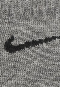 Tessuto grigio lavorato a maglia con un prominente logo swoosh nero della Nike. La texture appare morbida con un motivo di filato misto.