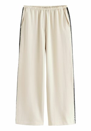 Krémové široké nohavice s elastickým pásom a čiernym cikcakovým lemom pozdĺž vonkajších švov, so stranovými vreckami.