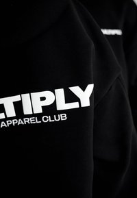 Tessuto nero con grande scritta bianca "ETIPLY" e testo più piccolo "APPAREL CLUB" stampato su di esso, che mostra parte di un indumento.