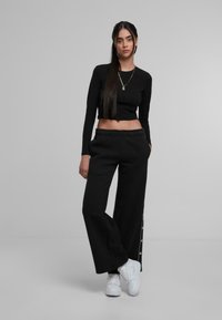 Črn dolgi rokav krojen top, v kombinaciji z širokimi črnimi trenirkami z gumbnimi zaprtji na straneh in zvezdnimi detajli, dopolnjen z belimi supergami.