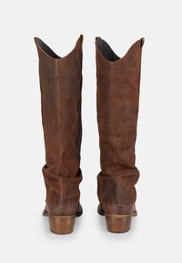 Bruine suede kniehoge laarzen met een slouchy ontwerp, puntige toppen en gestapelde houten hakken. Zachte textuur, schone stiksels goed zichtbaar.