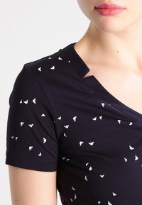 Mörkblå t-shirt med korta ärmar som har ett mönster av små vita trianglar. Subtil design vid halsringningen, mjuk bomullstextur.