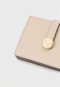 Bézs színű bőr pénztárca sima felülettel, arany patentos záródással és rendezett varrással a széleken.