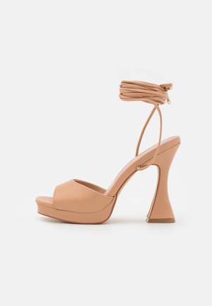 Sandales à talons ouverts beige avec une semelle plateforme et un talon sculpté unique. Comprend une bride de cheville texturée avec des liens.