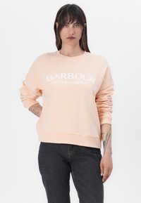 Párducsávos anyagból készült, barack színű kapucnis pulóver, kerek nyakkal, hosszú ujjakkal, a közepén fehér "BARBOUR INTERNATIONAL" logóval.