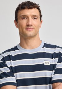 Randig kortärmad skjorta i marinblått och ljusblått, med rund halsringning och en liten logomärke på bröstet. Tillverkad av bomull.