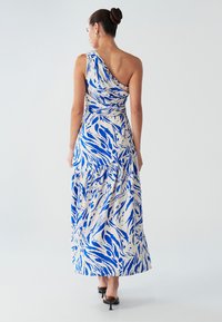 Robe longue à une épaule, avec un motif abstrait bleu et blanc, jupe à volants, et dos drapé. Texture de tissu lisse.