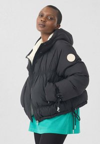 Zwarte donsjack met capuchon, contrasterende witte binnenkant, ritssluiting, elastische manchetten en trekkoorden aan de zoom. Voorzien van een logopatch.