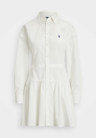 Valge nööbiga särgimekk pikkade varrukatega, koos kogutud seeliku ja istuva taljega. Rinnal on väike tumesinine logo.