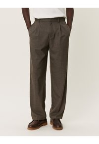 Brown checkered trousers with a relaxed fit, pleated front, side pockets, and a waistband. Paired with dark brown shoes.