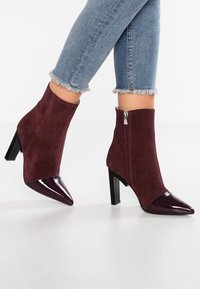 Bottines bordeaux à tige basse en daim, bout pointu en cuir verni brillant et détail zippé. Talon stiletto et tissu texturé.