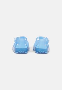 Blue transparent sandals with a sleek design, open sides, adjustable strap, and textured soles, featuring the brand name "igor" on the back.