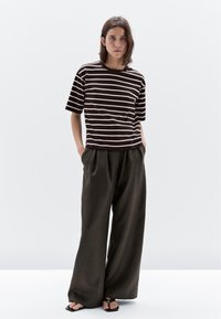 Brun og hvid stribet kortærmet skjorte parret med løse mørke bukser, der har en afslappet pasform og glat stof. Flade sandaler fuldender looket.