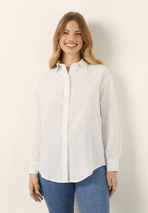 Hvidt linned skjorte med lange ærmer, knap-ned krave, buet kant og løs pasform. Sammen med blå denim jeans.