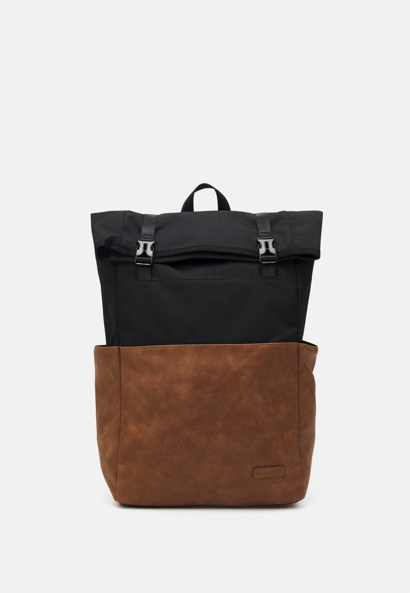 Sac à dos avec dessus en tissu noir et bas en cuir synthétique marron, rabat avant sécurisé par deux boucles noires et poignée de transport au centre en haut.