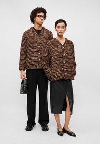 Dva modely v zhodujúcich sa textúrovaných bordových svetroch s gombíkmi, v kombinácii s čiernymi nohavicami a koženou sukňou, doplnené doplnkami.