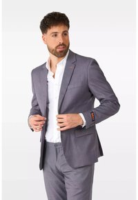 Helles graues Blazer mit schlanker Passform, kombiniert mit einem weißen Hemd. Es verfügt über ein gesticktes Logo am Ärmel und eine einzelne Brusttasche.