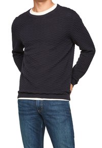 Marynarski teksturowany sweter w prążki z białym okrągłym dekoltem, z dopasowanym dołem, noszony na jasnoniebieskich dżinsach.