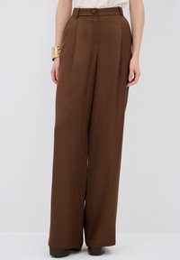Bruine, wijde broek van lichtgewicht stof. Heeft een hoge taille, een enkele knoopsluiting en plooien aan de voorkant. Glad textuur.