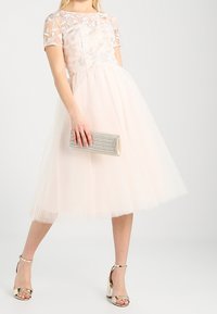 Pink tulle dress with a sheer, embroidered overlay, short sleeves, and a flared skirt. Paired with silver ankle strap heels and a clutch.