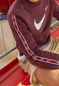 Maroon sweatshirt with white Nike logo, featuring textured fabric and contrasting stripes along the sleeves in red and white. Casual design.