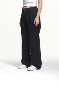 Black wide-leg cargo pants with multiple pockets, made from thick denim. Features a high waist and a loose fit, paired with white sneakers.