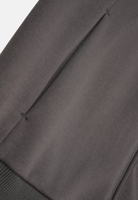 Tessuto in morbido cotone grigio con polsini a coste e dettagli di cucitura sottili. Presenta tasche laterali con un design snello.