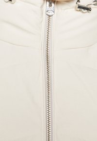 Giacca beige con zip, dotata di una cerniera argentata, texture liscia e pannelli trapuntati. Cordino regolabile nel colletto.