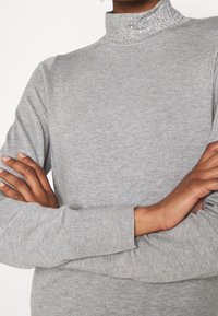 Szary golf wykonany z miękkiego materiału, z prążkowanym kołnierzem ozdobionym błyszczącymi akcentami oraz długimi rękawami.