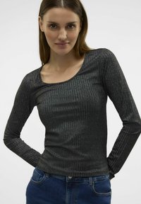 Zwarte lange mouw top met een geribde textuur en een ronde hals, gemaakt van een glanzend, rekbaar materiaal. Gecombineerd met blauwe jeans.