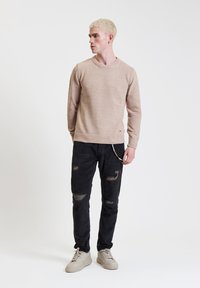 Jasno beżowy sweter z dzianiny o okrągłym dekolcie zestawiony z czarnymi spodniami z korduroy w stylu distressed. Noszone z jasnoszarymi trampkami.