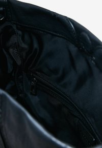 Schwarze Lederhandtasche mit einem glatten, strukturierten Innenfutter und einer Reißverschlusstasche für sichere Aufbewahrung. Keine sichtbaren Verzierungen.