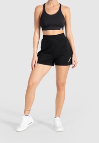 Black sports bra with thick straps paired with black athletic shorts, both made from soft fabric. White sneakers with visible branding.