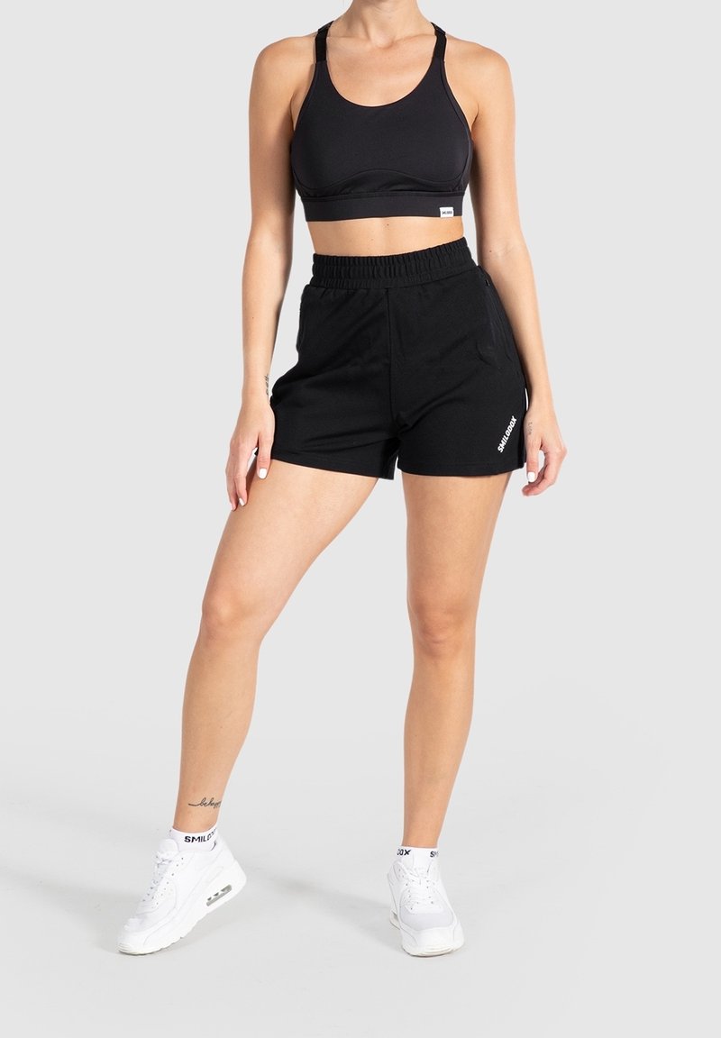 Black sports bra with thick straps paired with black athletic shorts, both made from soft fabric. White sneakers with visible branding.