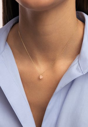 Goldkette mit einer zarten Kette, die einen kleinen, herzförmigen, rosa Edelsteinanhänger zeigt, präsentiert vor einem hellblauen Hemd.