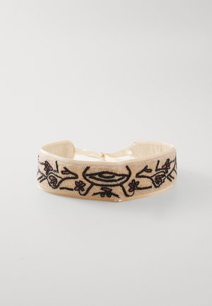 Broderad hårband med en beige tygbas, prydd med svarta blommönster och röda accenter, fäst med ett band.